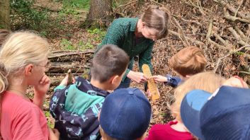 Umweltbildnerin und Kinder stehen im Wald und ein Thermometer wird betrachtet